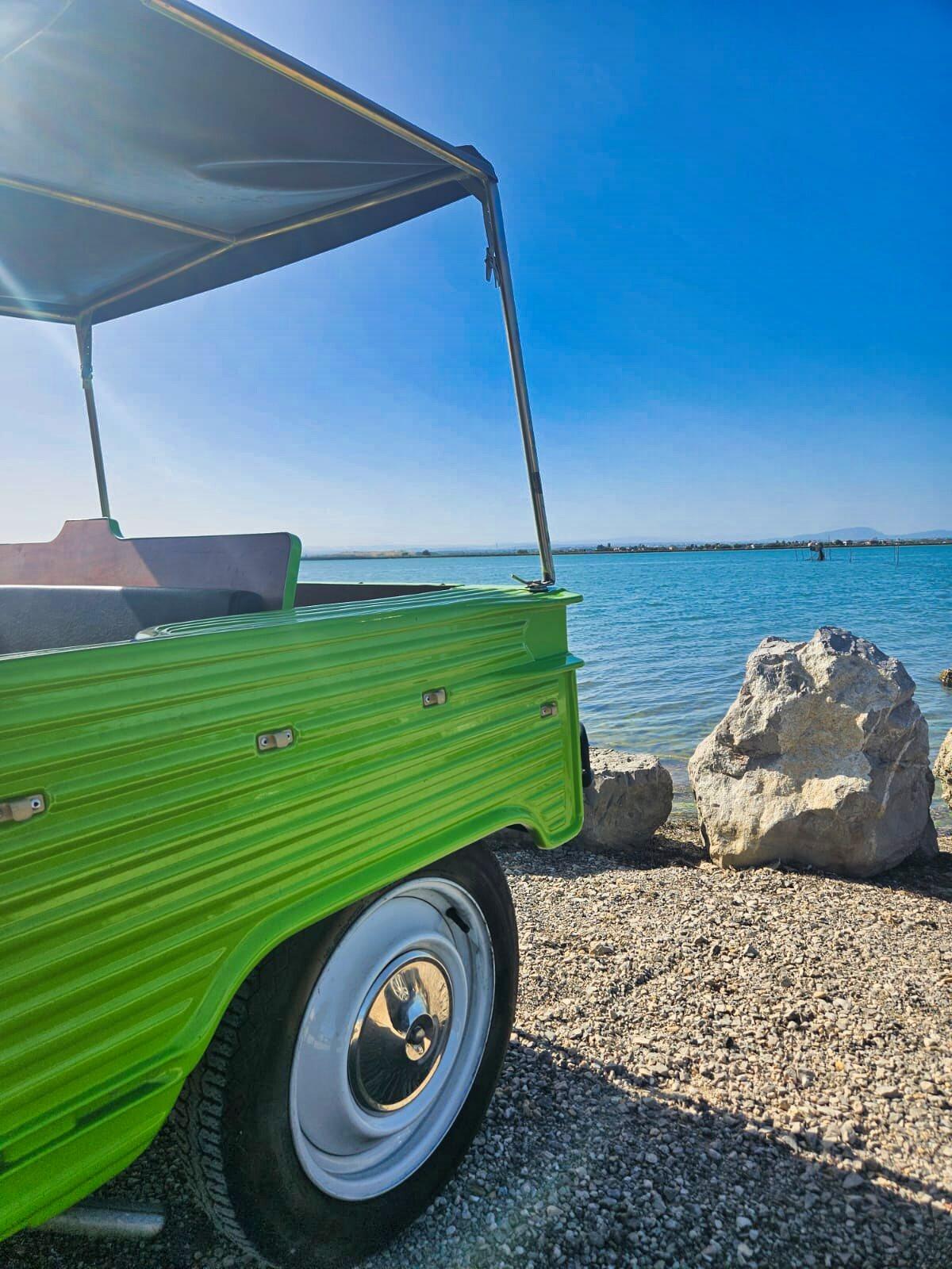 Arrière d'une Citroën Méhari vert fluo au bord d'un étang, rochers et ciel bleu